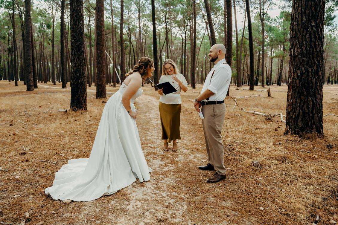 A bride and groom with their officiant in a forest clearing during their loveiam wedding ceremony, sharing smiles.